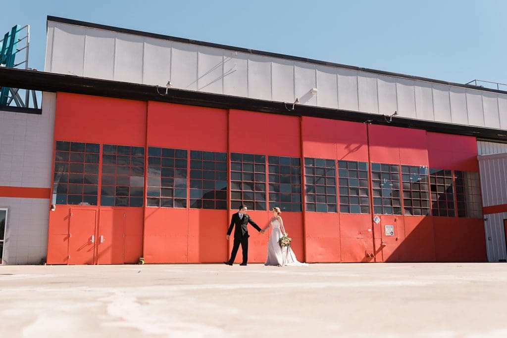 bride and groom in front of hangar doors