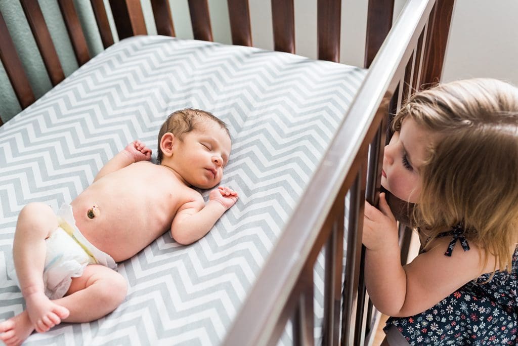 big sister looking at newborn baby in crib 