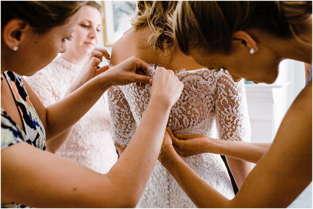 bridesmaids buttoning up brides dress