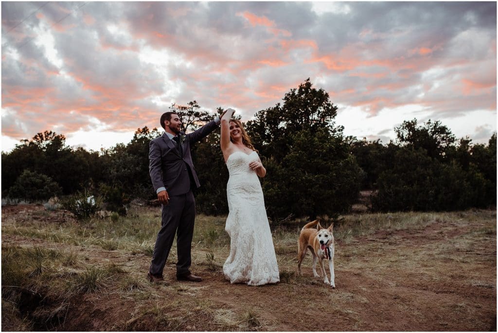 bride and groom dancing at sunset with their dog