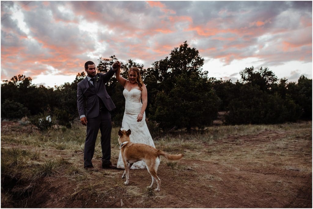 bride and groom dancing at sunset with their dog