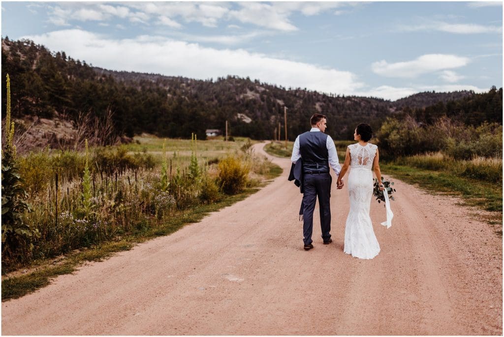 bride and groom walking hand in hand down a dirt road in the mountains