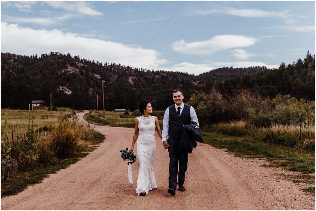 bride and groom walking hand in hand down a dirt road in the mountains