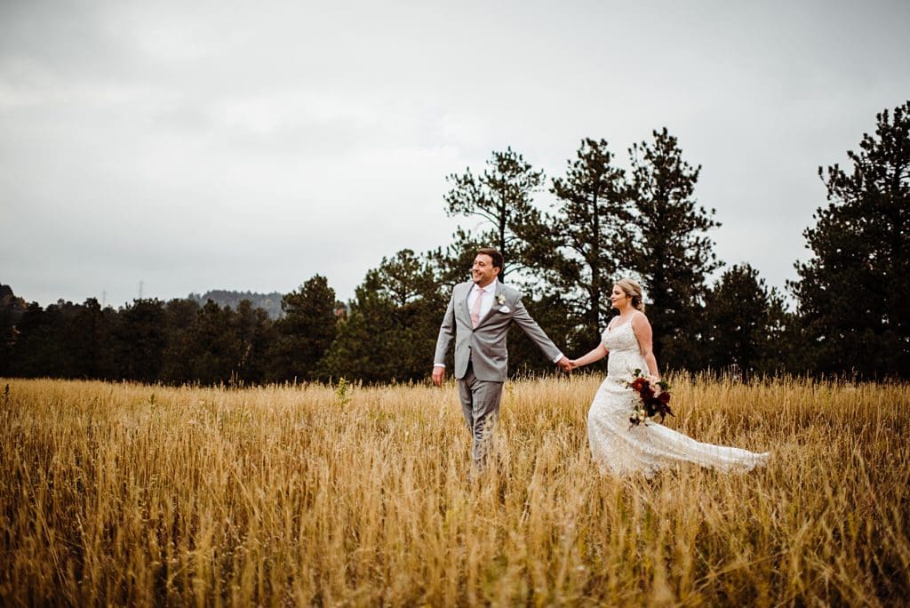 bride and groom walking through a field in golden