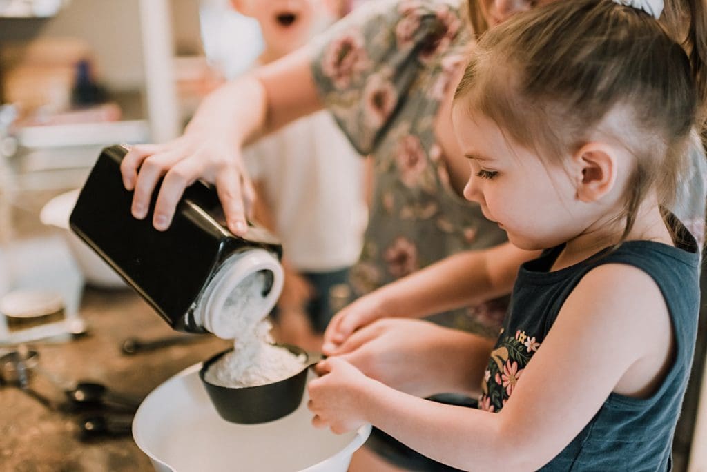 little girl holding measuring cup while making waffles with mom