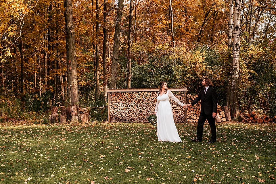 bride and groom walking in front of wood pile