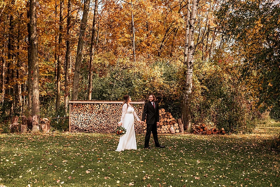 bride and groom walking in front of wood pile