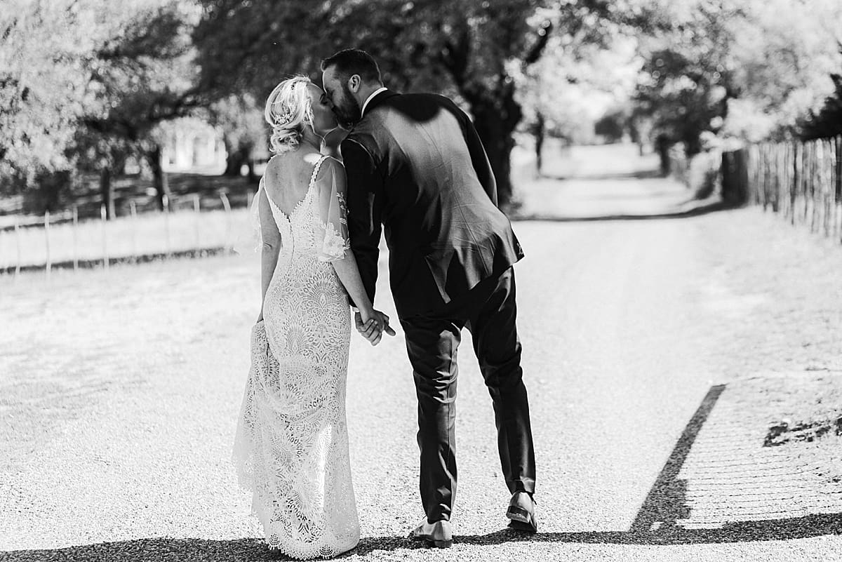 black and white image of bride and groom walking and kissing from behind