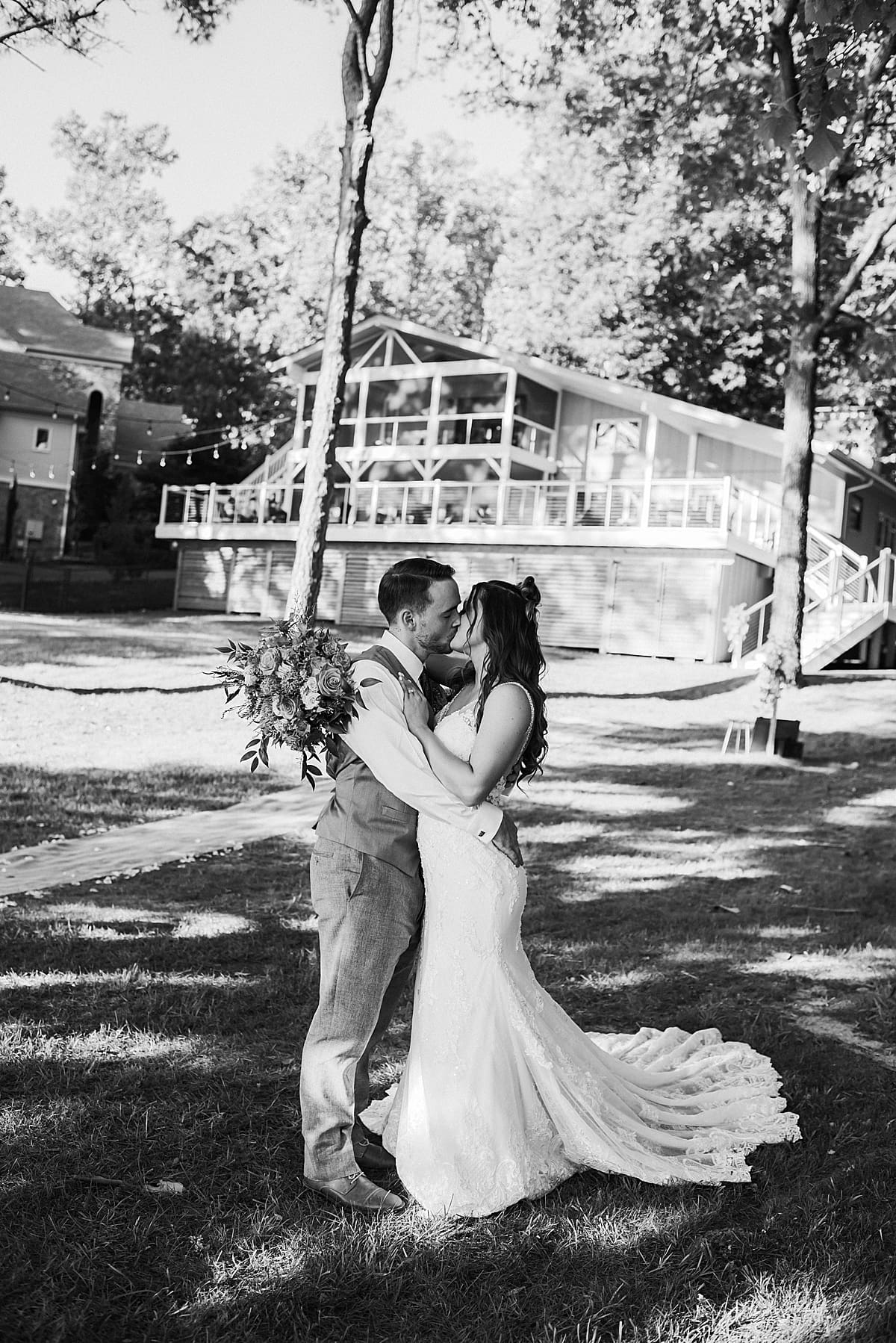 bride and groom kissing in front of lake house
