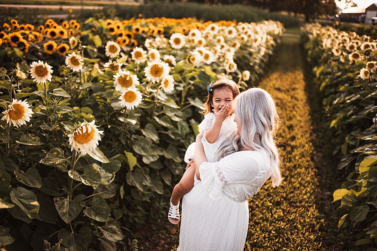 mom and baby girl snuggling in a field of sunflowers