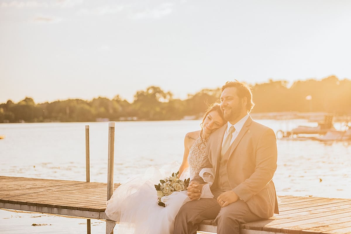 bride and groom sitting together on the pier at sunset