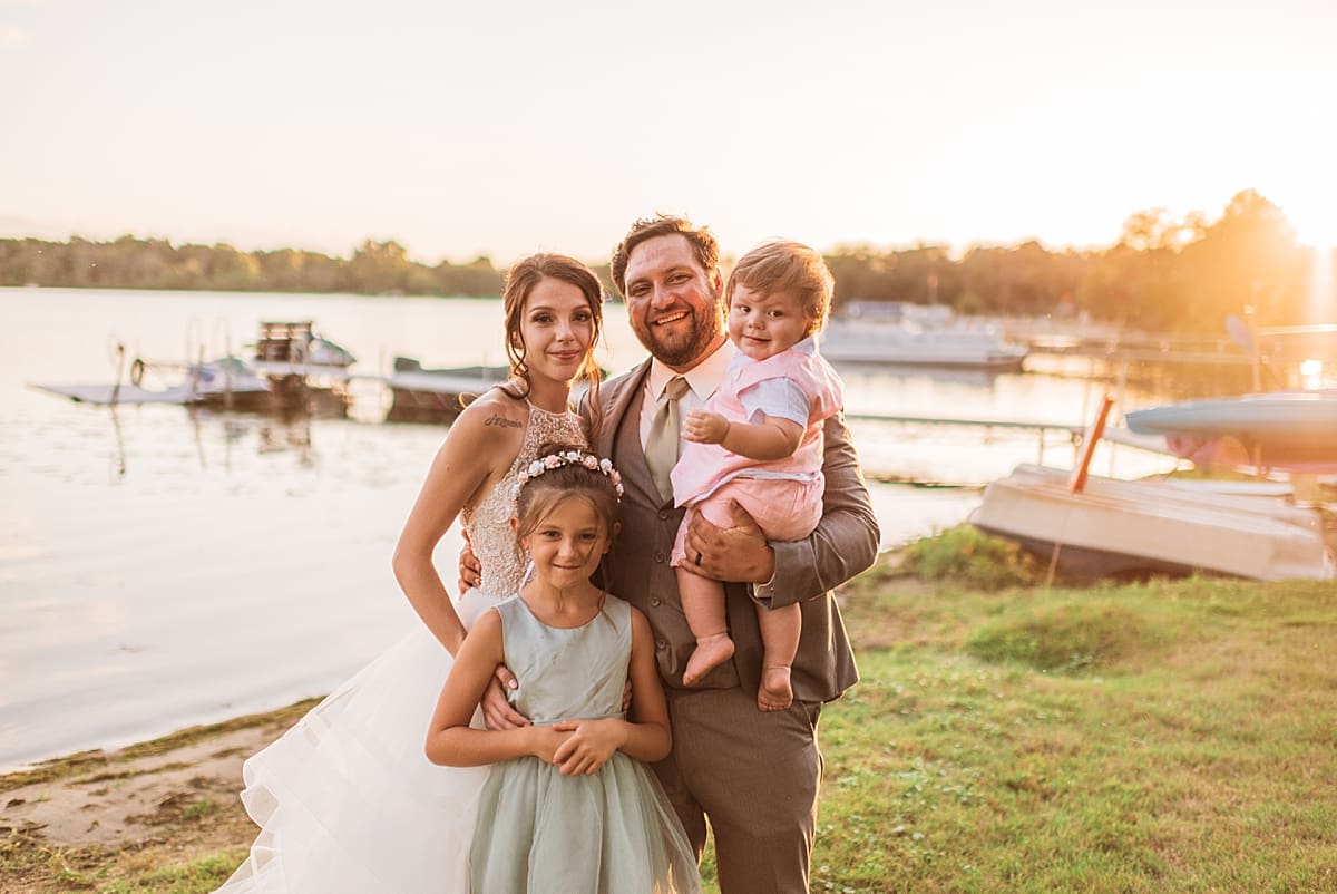 bride and groom with their kids in front of the lake at sunset