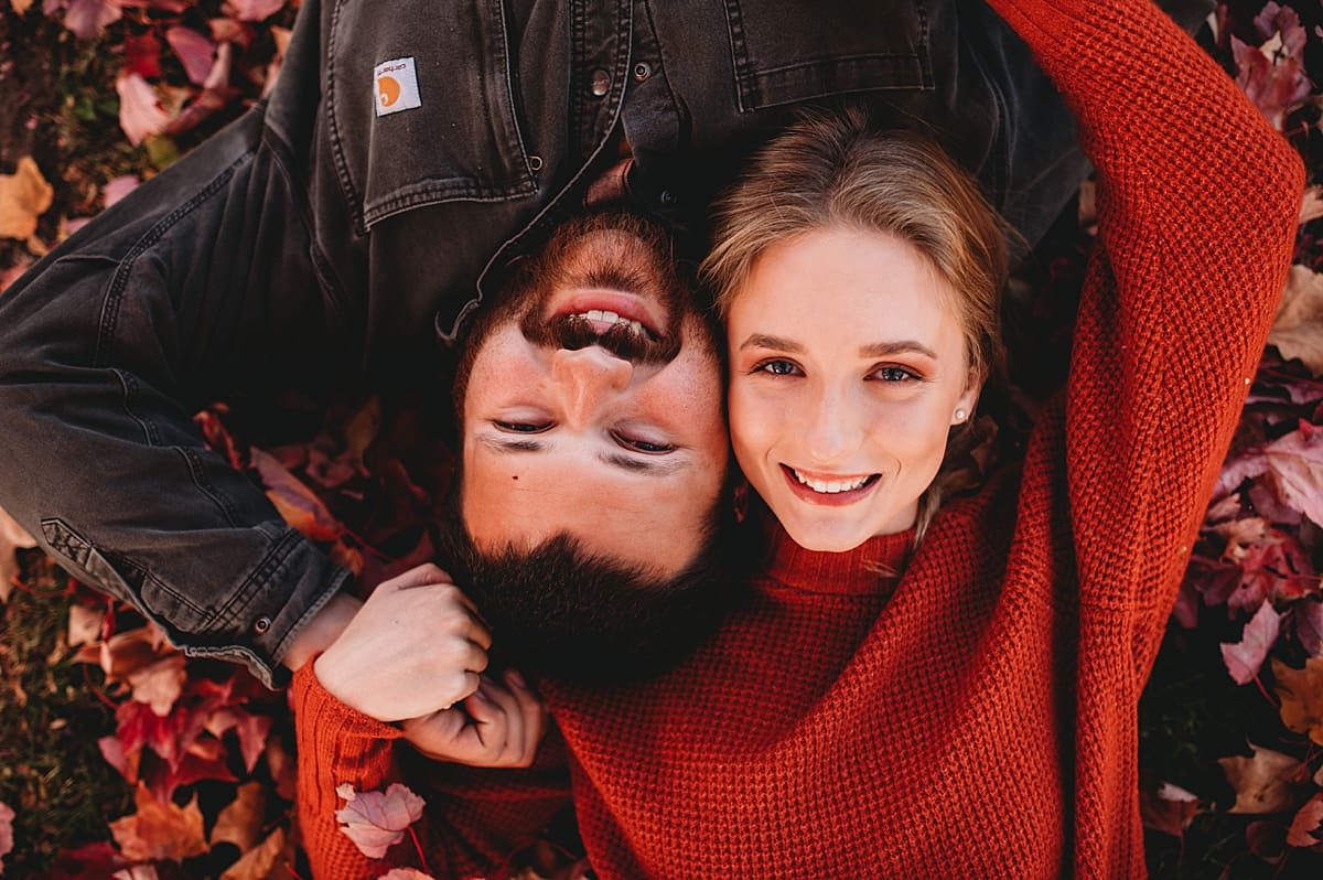 couple laying together in fall leaves pile
