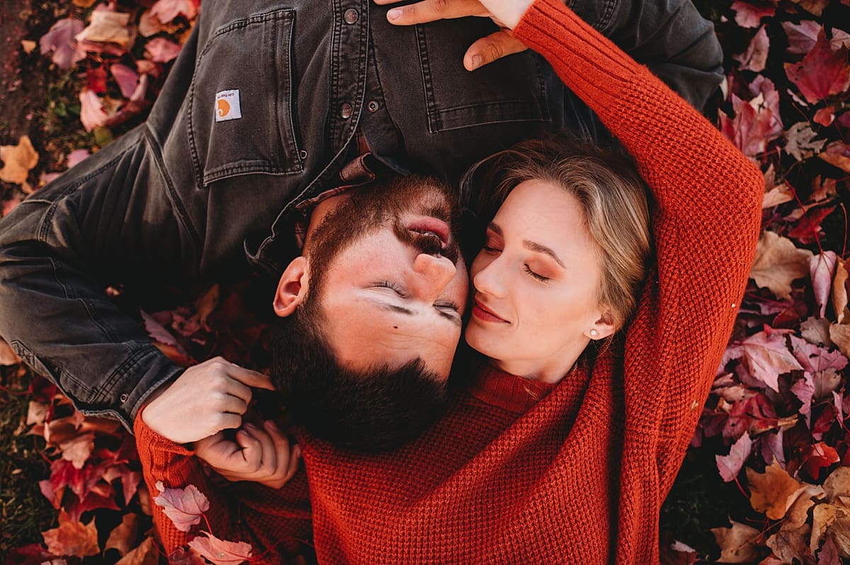 couple laying together in fall leaves pile