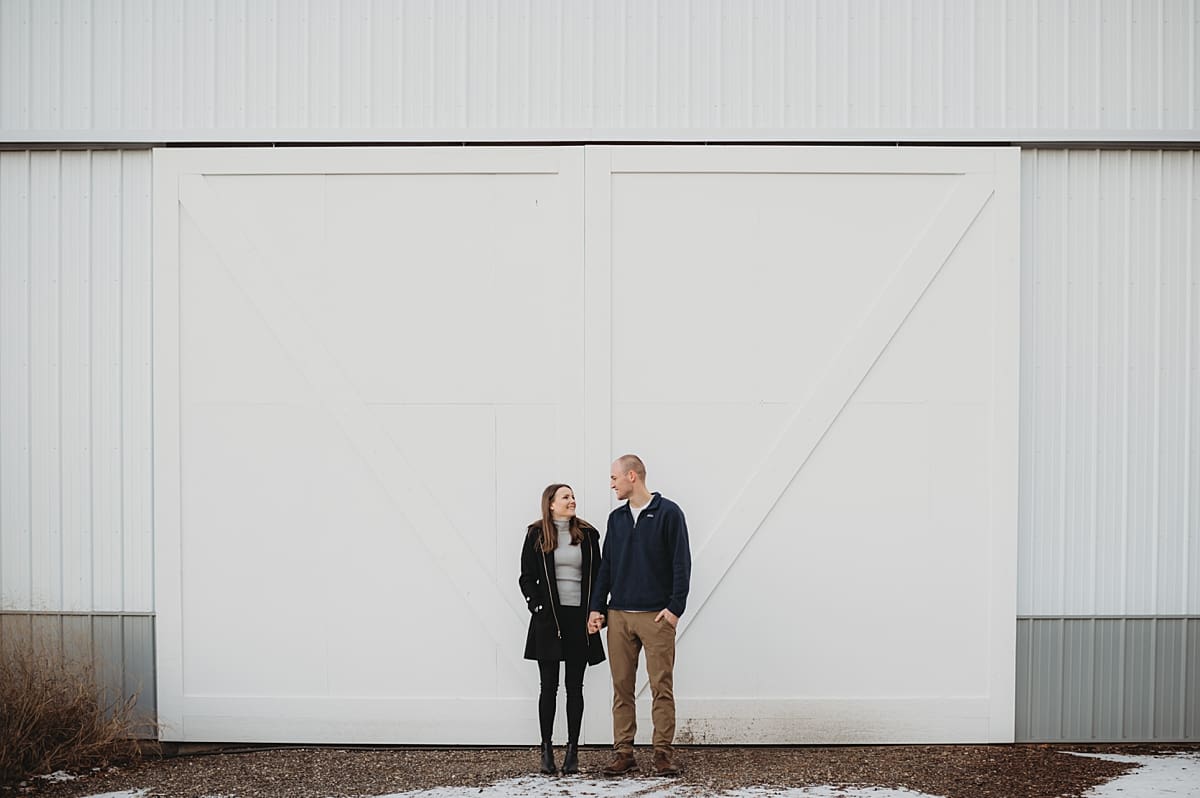 couple holding hands and smiling in front of large barn doors
