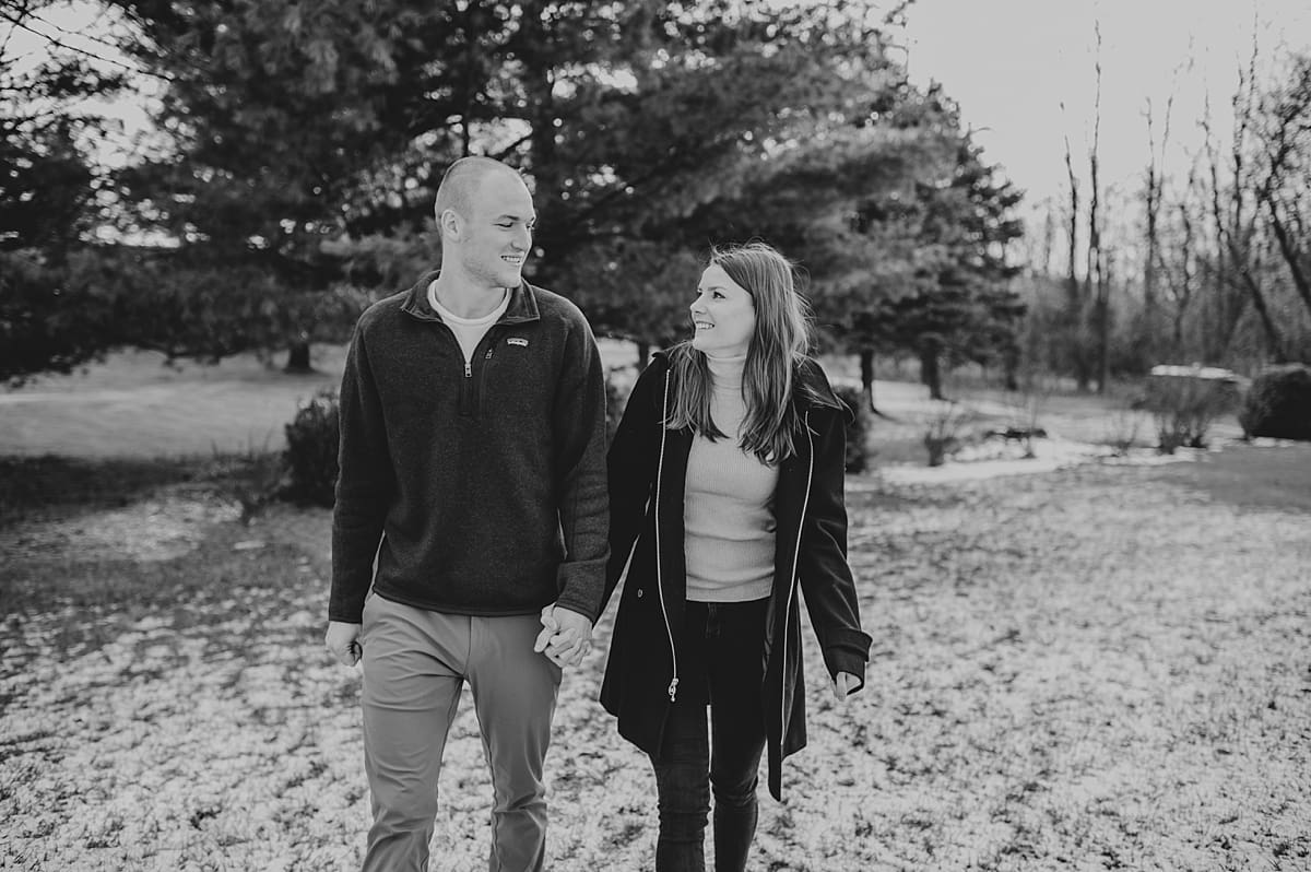 black and white image of couple walking together in snow for engagement session