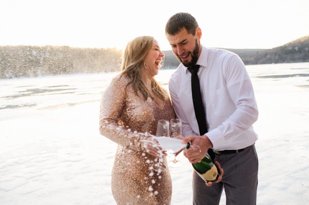 popping champage at an engagement session on a frozen lake