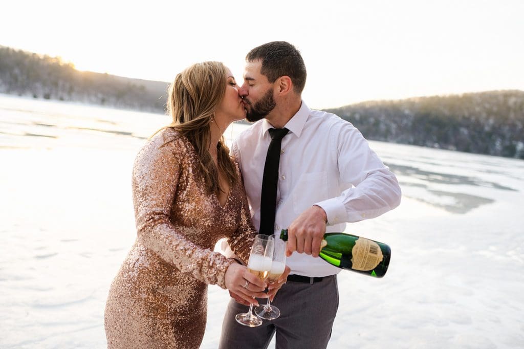 popping champage at an engagement session on a frozen lake