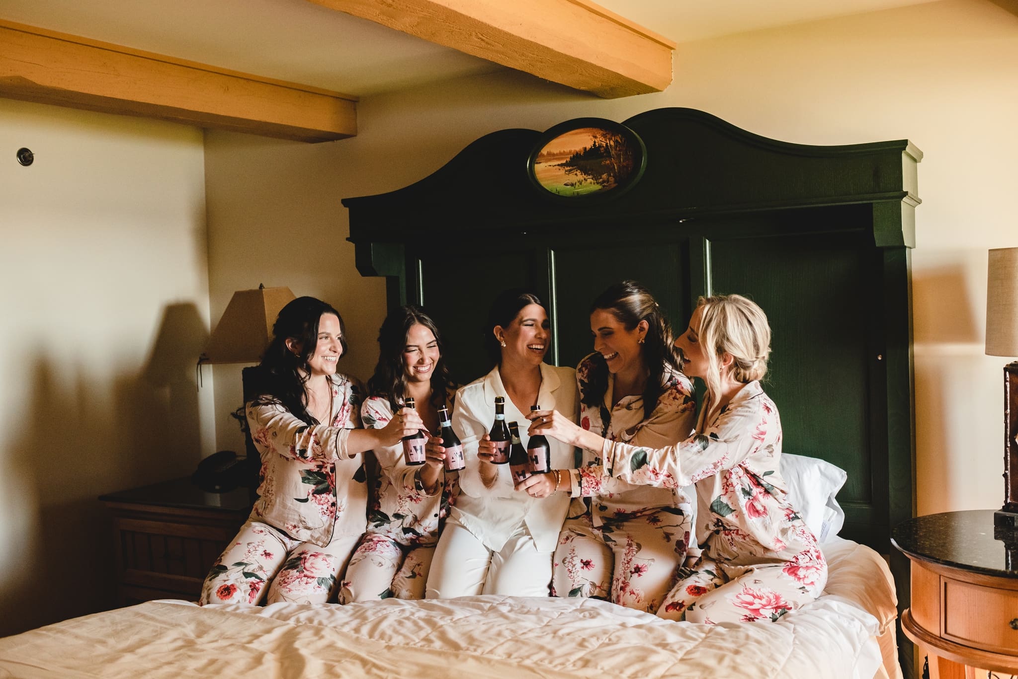 bride with bridesmaids on the bed with champaigne