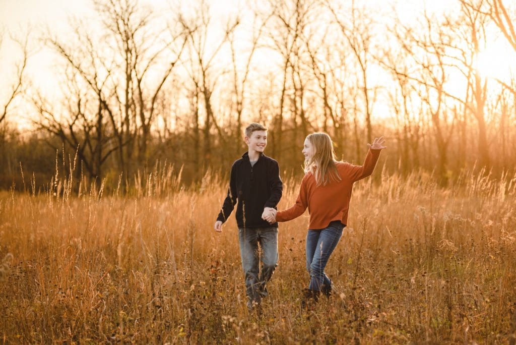 siblings holding hands and running together in a field for family photos