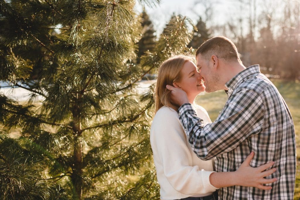 couple kissing next to green evergreen tree