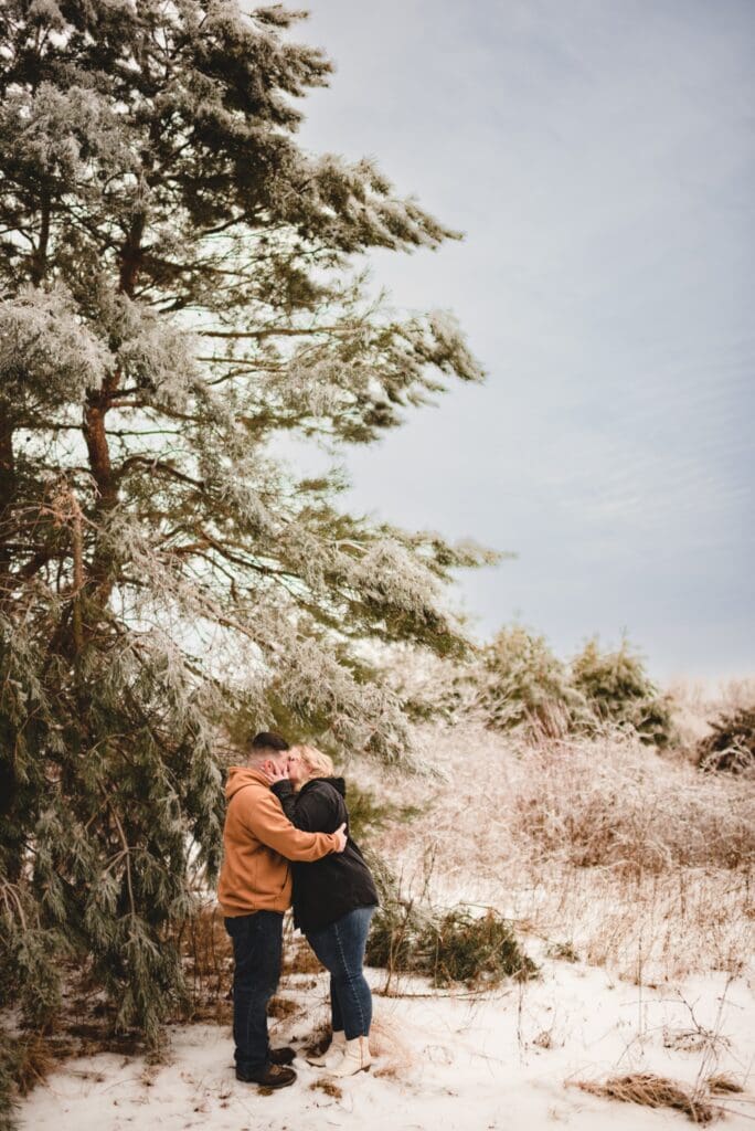couple kissing in front of tall evergreen
