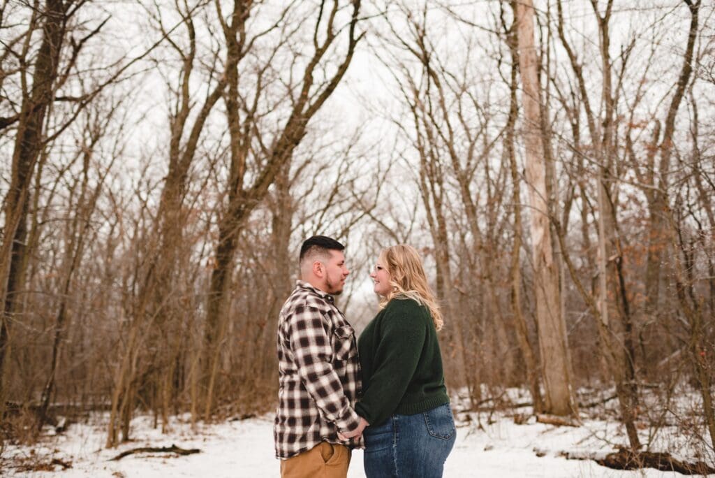 engaged couple holding hands looking at each other in the snow