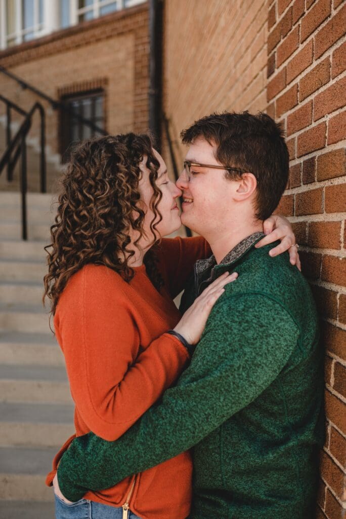 man and woman leaning against brick wall for a kiss