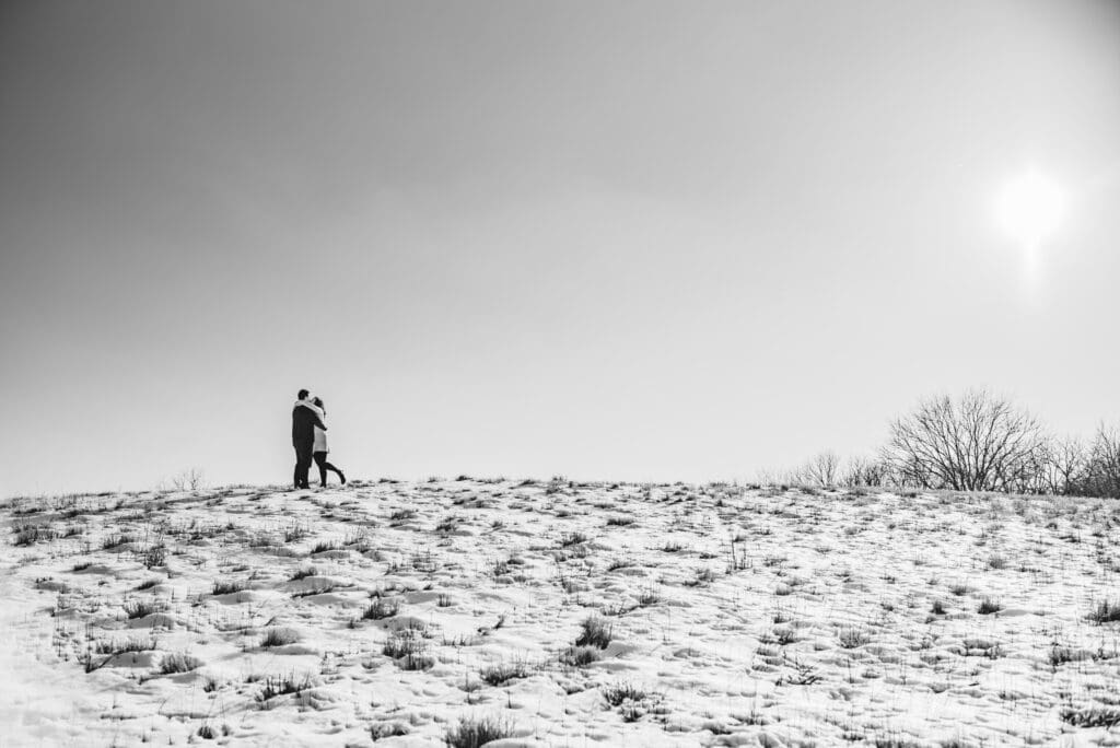 engaged couple kissing on top of a snowy hill