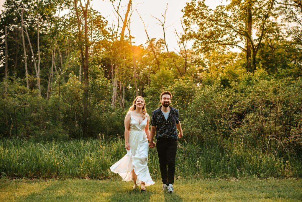engaged couple running together in a field with trees