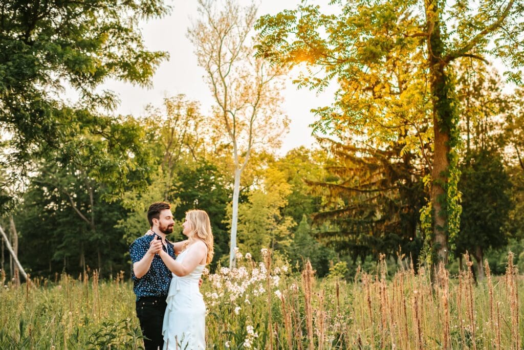 engaged couple dancing together in a field with trees