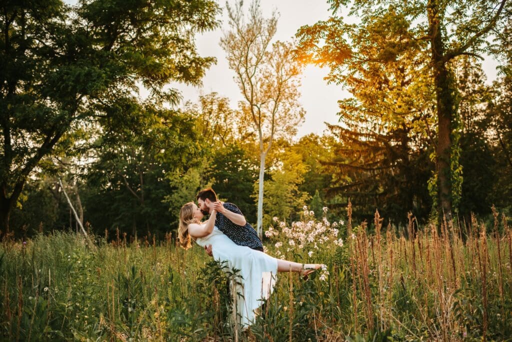 engaged couple dancing together in a field with trees