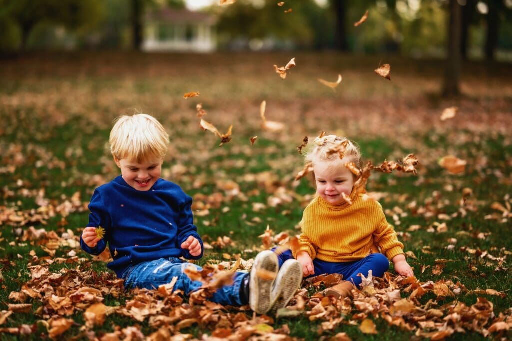toddlers playing in fall leaves at the park